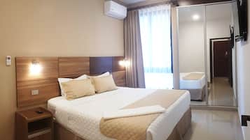 A modern hotel room with a large bed, bedside tables, an air conditioning unit, a mirror, and a view of the outside.