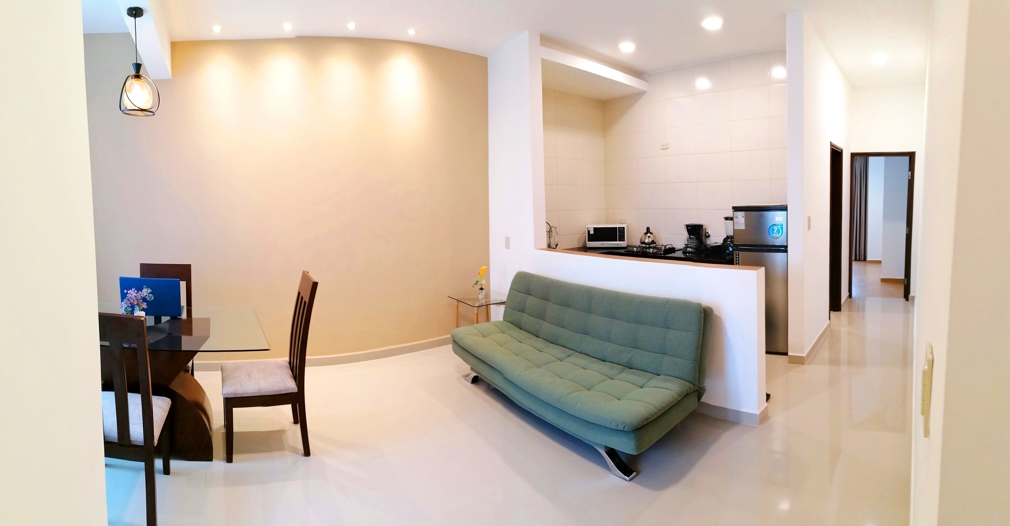 Un salon moderne avec un canapé vert, une table à manger avec des chaises et un coin cuisine équipé d’un four à micro-ondes et d’une machine à café.