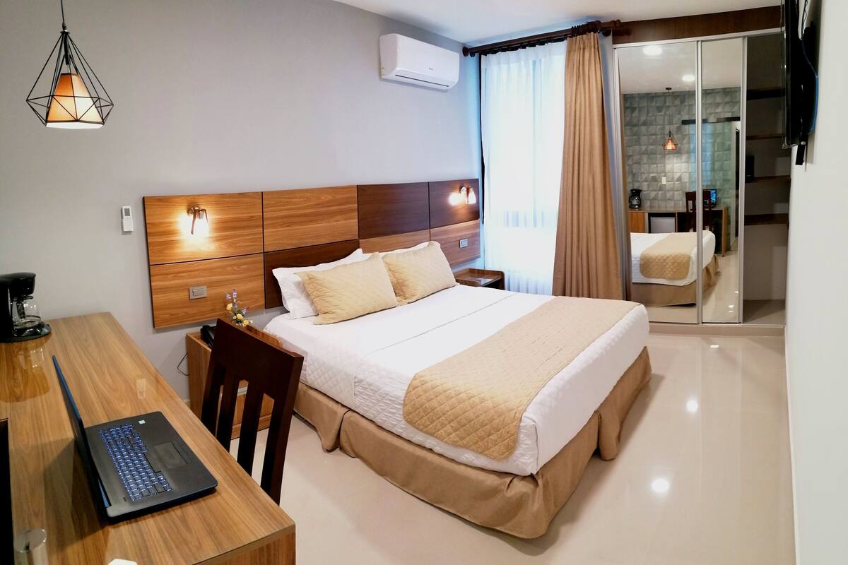 Une chambre d’hôtel comprenant un lit, un bureau avec un ordinateur portable, une chaise, une table de chevet et un téléviseur fixé au mur.