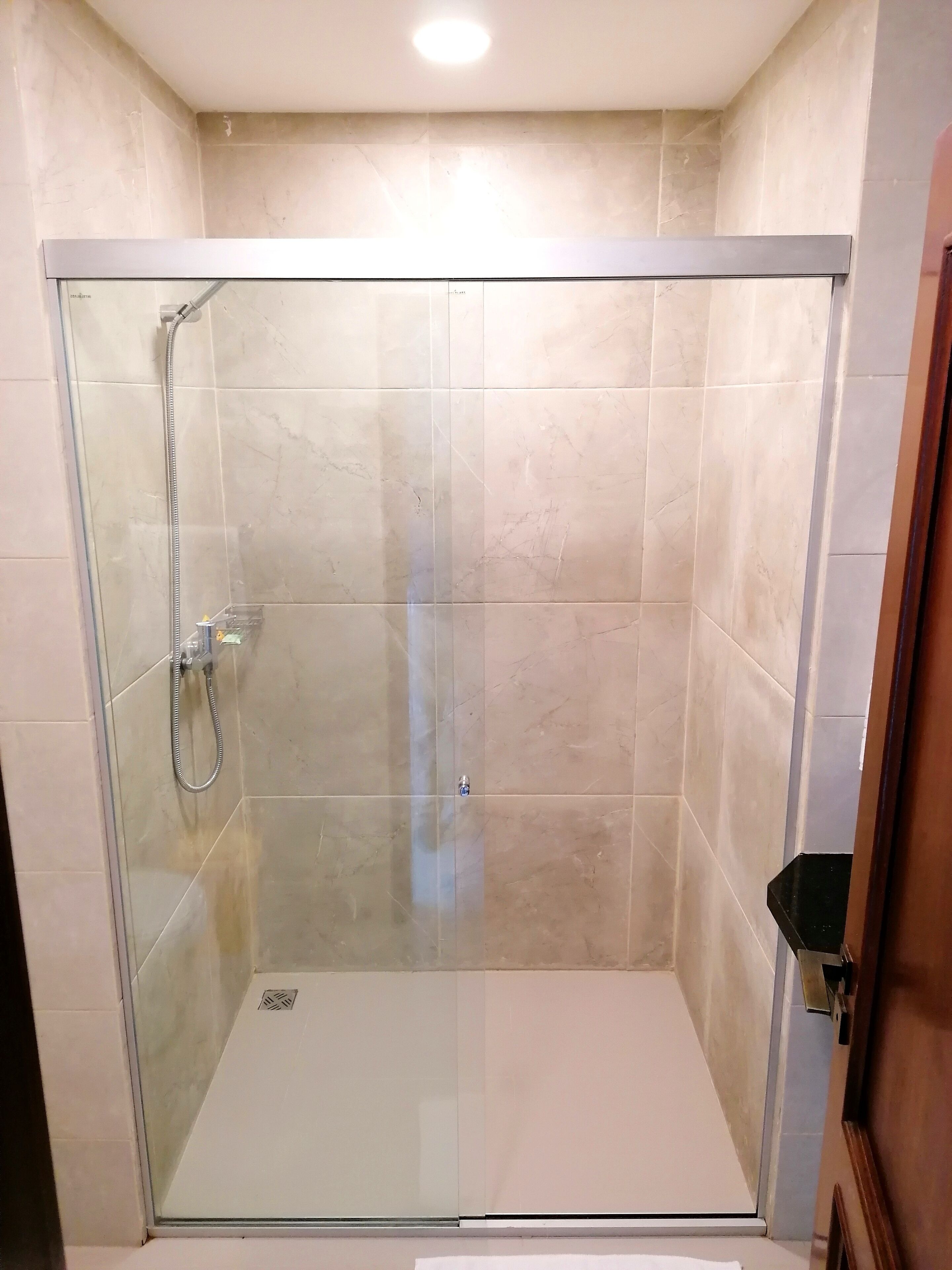 Cabina de ducha con paredes de vidrio, cabezal de ducha de mano y llave de control.