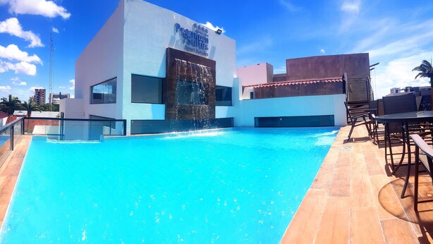 A rooftop pool with a water feature, surrounded by modern buildings and a clear sky.