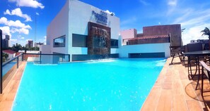 Una piscina en la azotea con fuente, rodeada de edificios modernos y un cielo despejado.