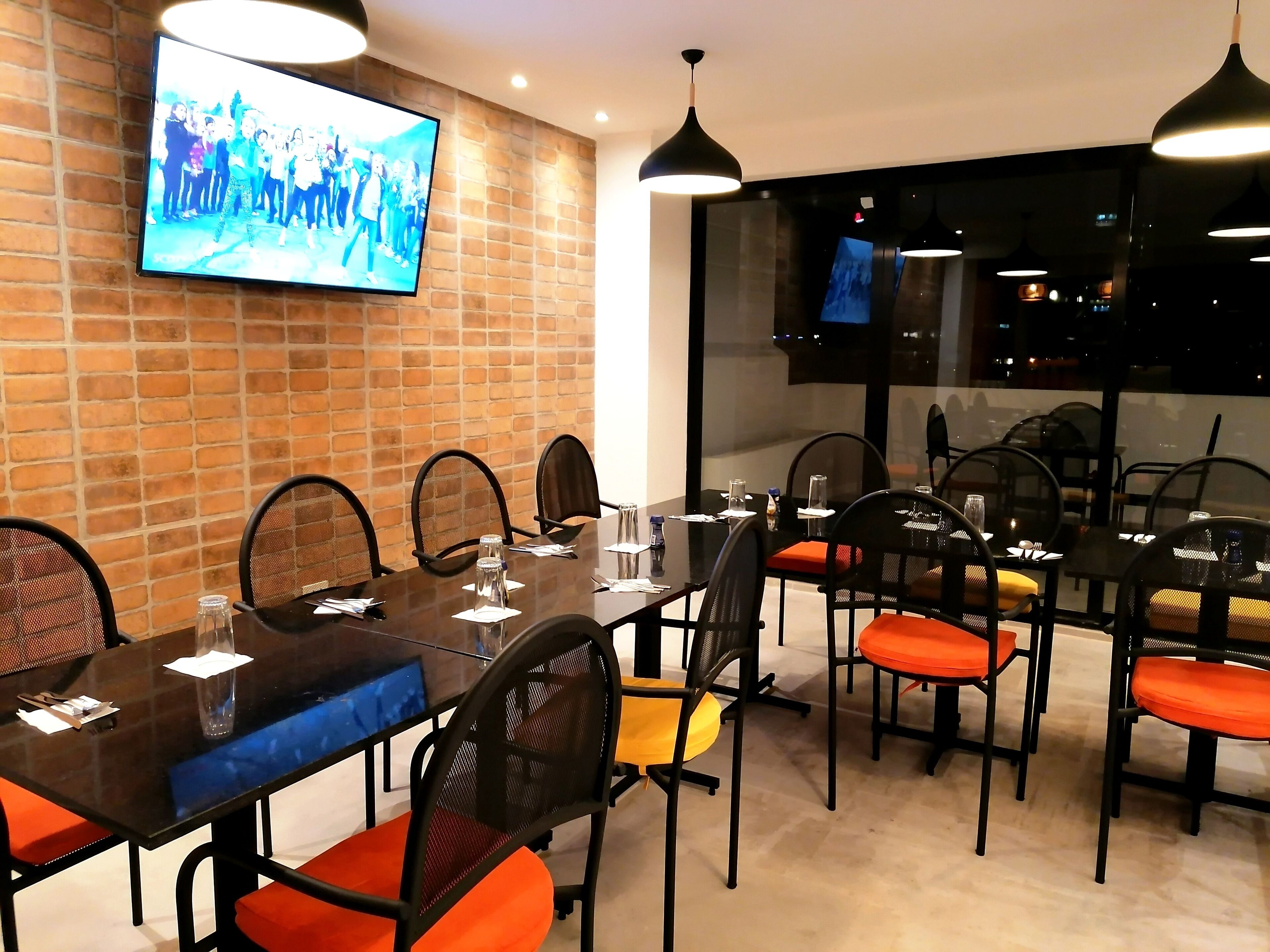 A conference room with a brick wall, a large flat-screen TV, and modern pendant lighting.