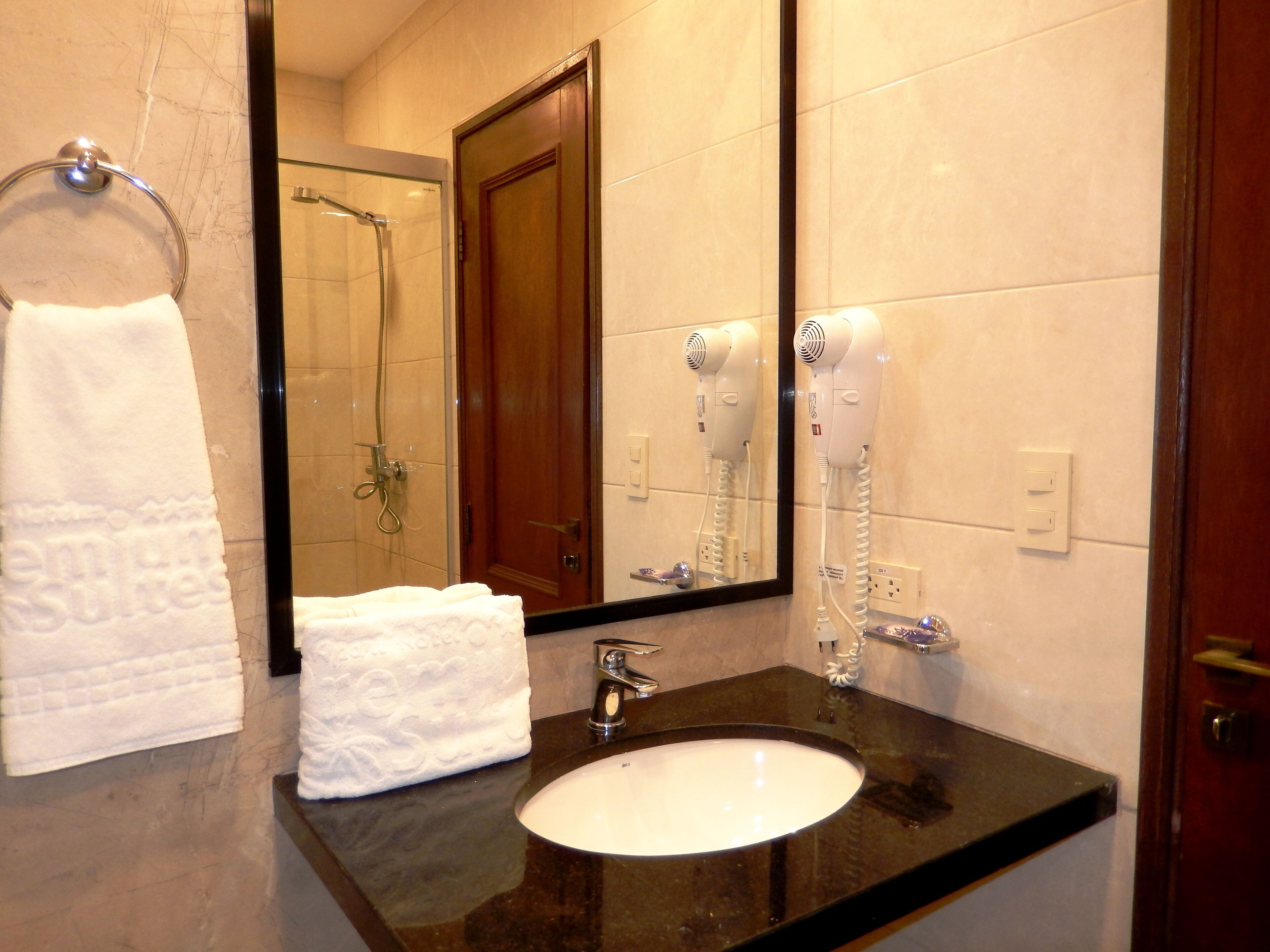 Baño con lavamanos, toallero y espejo que refleja la zona de la ducha.