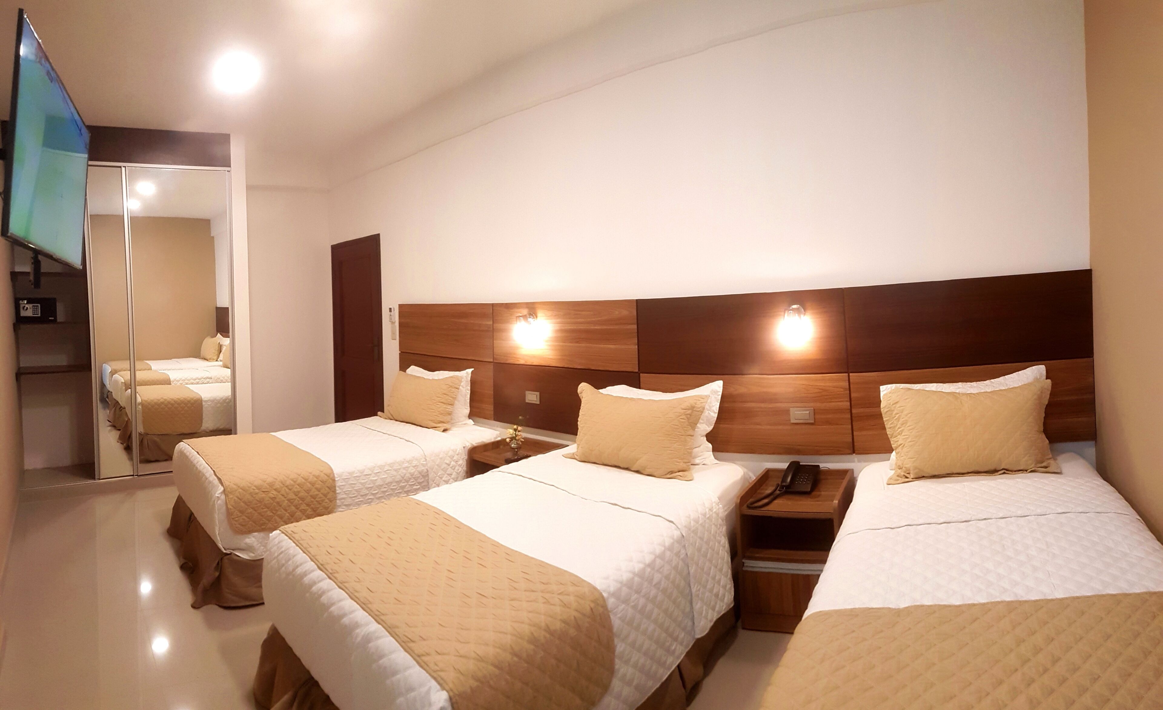 Een hotelkamer met twee bedden, een houten hoofdeinde, nachtkastjes met lampen en een spiegel.