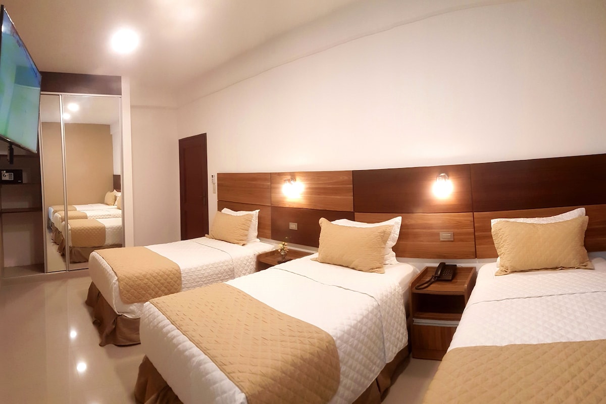 A hotel room with two beds, a wooden headboard, bedside tables with lamps, and a mirror.