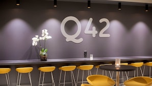Un espace d’accueil avec une grande enseigne « Q42 », un vase rempli de fleurs blanches et des tabourets de bar jaunes.