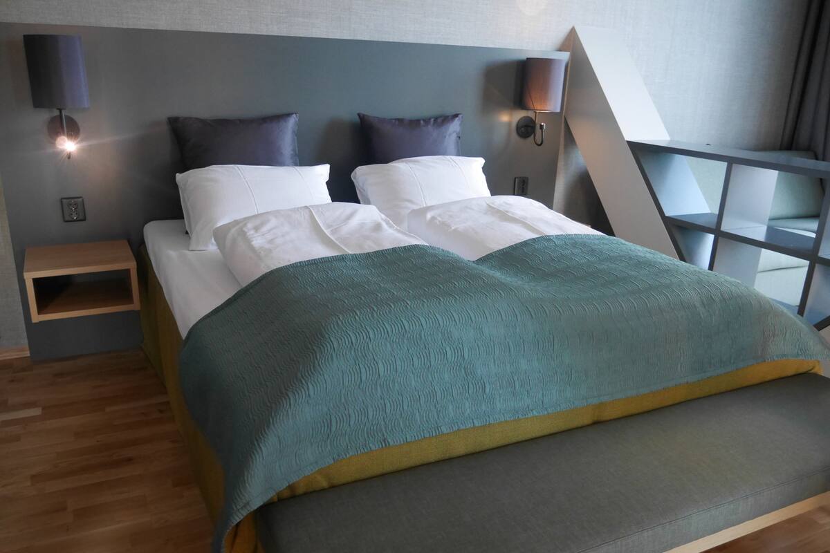 A modern bedroom with a bed, two bedside lamps, a nightstand, and a view of the outside.
