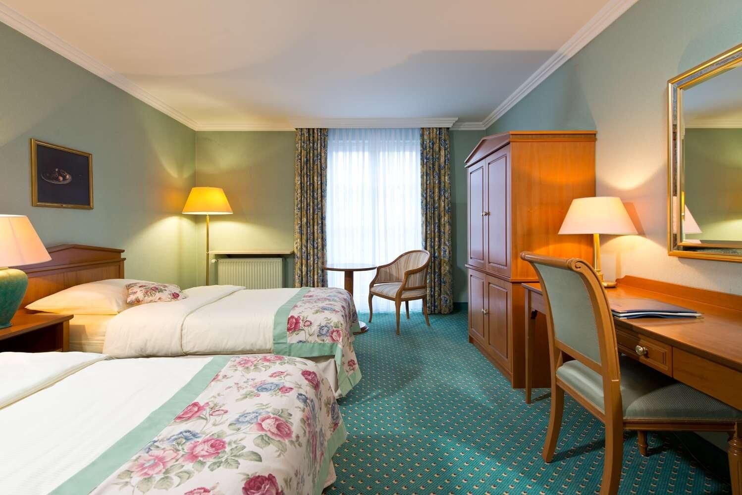 A hotel room with two beds, a desk, a chair, a wardrobe, and a window with curtains.