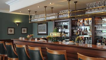 A bar area with a wooden counter, bar stools, and a glass display shelf.