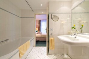 A modern bathroom with a bathtub, a sink, and a mirror. - Hotel Am Schlosspark (Gotha)
