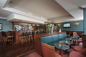 Una zona de bar con una barra larga, varios taburetes, una sala de estar con cojines y varias mesas redondas pequeñas con sillas.