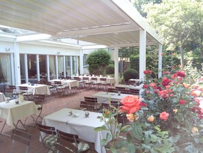 An outdoor patio with tables and chairs, surrounded by a garden with roses. - Hotel Am Schlosspark (Gotha)