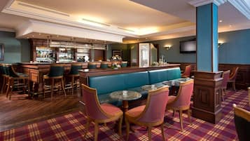 A bar area with a long counter, multiple bar stools, and a seating area with a blue bench and round tables.