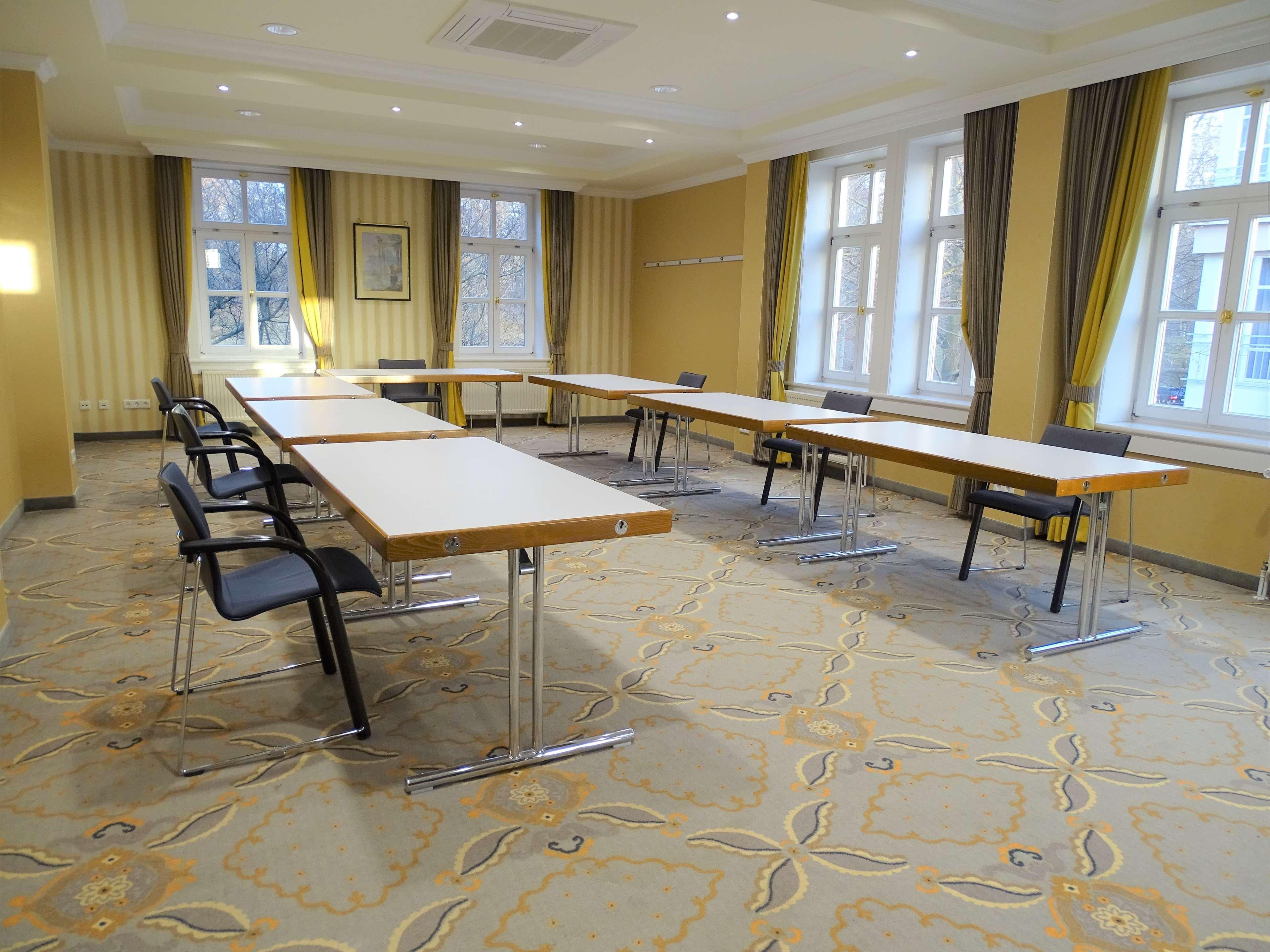 A conference room with long tables and chairs, large windows with curtains, and patterned carpet.