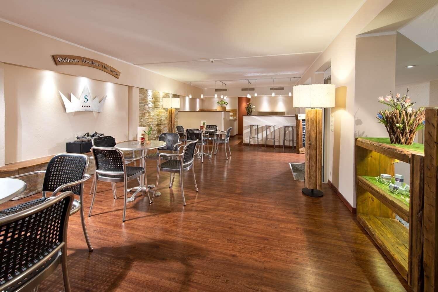 Un vestíbulo de hotel con mostrador de recepción, zona de estar con mesas y sillas, y una exhibición decorativa de plantas.