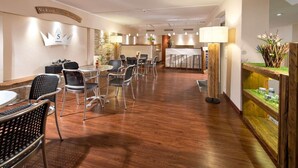 A hotel lobby with a reception desk, seating area with tables and chairs, and a decorative plant display. - Hotel Am Schlosspark (Gotha)