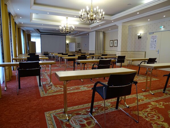 Un salón de conferencias con mesas y sillas, una araña y una alfombra estampada.