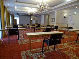 A conference room with tables and chairs, a chandelier, and a patterned carpet.