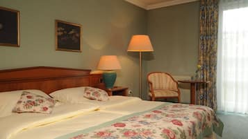 A hotel room with a bed, two lamps, a chair, a table, and a window with curtains.