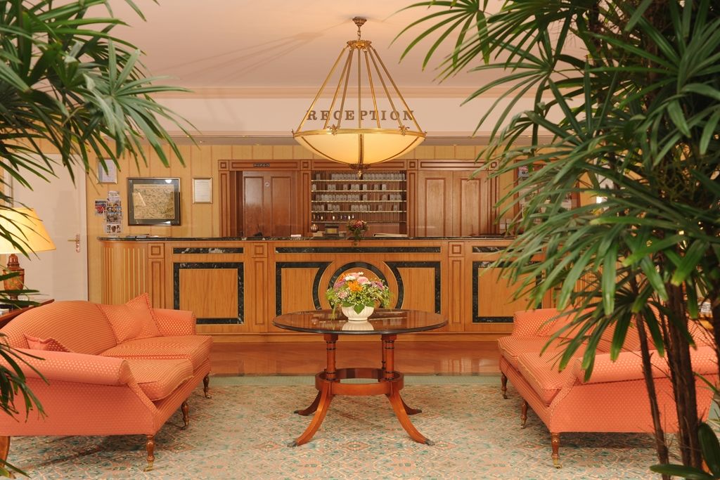 Un área de recepción con una araña, dos sofás, una mesa con un florero y armarios de madera.