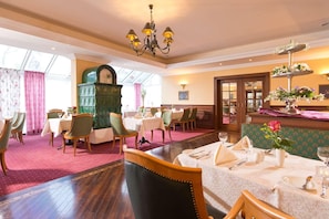 A dining area with round tables, chairs, a green clock, and a chandelier. - Hotel Am Schlosspark (Gotha)