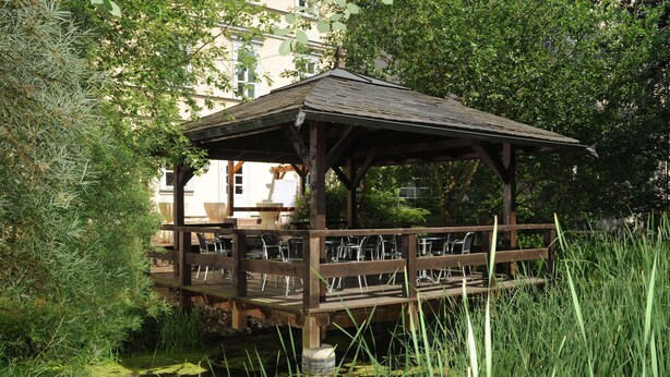 A wooden gazebo with a roof, surrounded by lush greenery and a pond. - Hotel Am Schlosspark (Gotha)