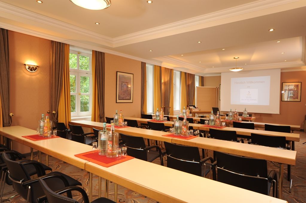 A conference room with long tables, chairs, and a projector screen displaying a presentation.