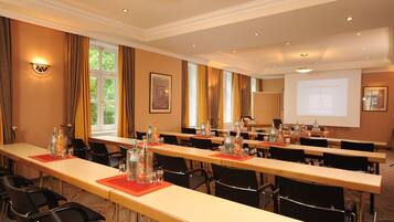 A conference room with long tables, chairs, and a projector screen displaying a presentation.