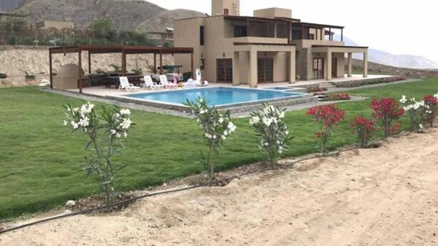 Una casa moderna de dos pisos con piscina, terraza cubierta y vistas a las montañas.