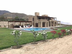 Une maison moderne à deux étages, dotée d’une piscine, d’un patio couvert et offrant une vue sur les montagnes.