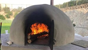 Un horno de piedra con frente abierto, fuego ardiendo en su interior y una pared de piedra al fondo.