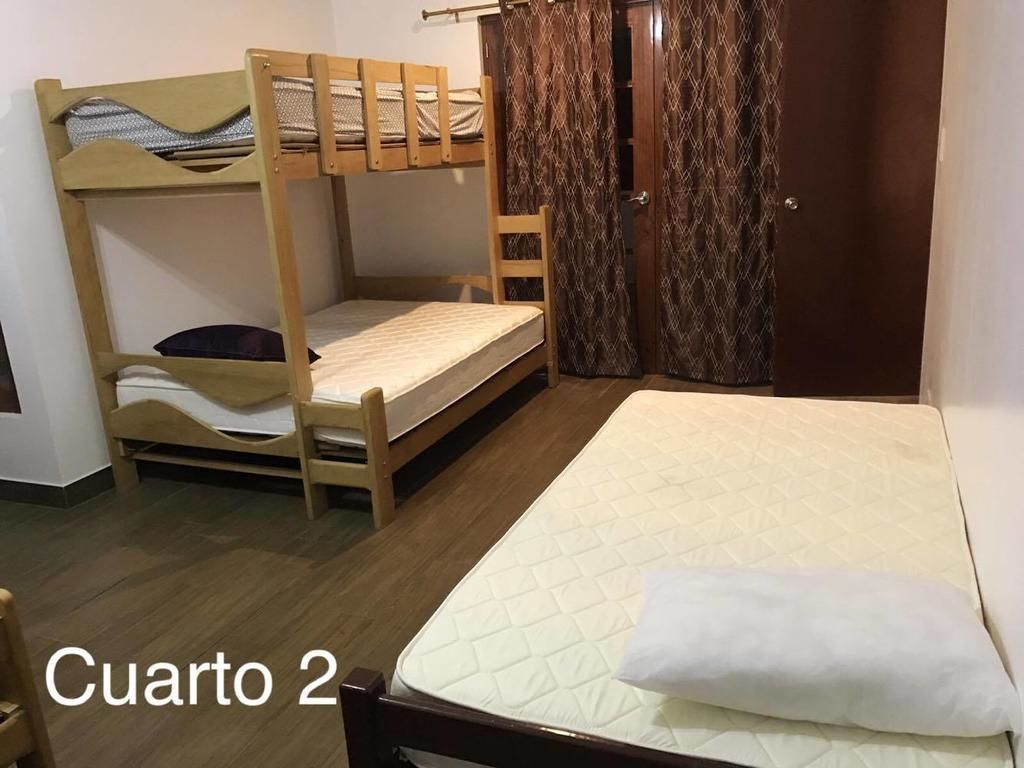 Una habitación con una cama litera, una cama individual, una silla de madera y una puerta con cortinas estampadas.