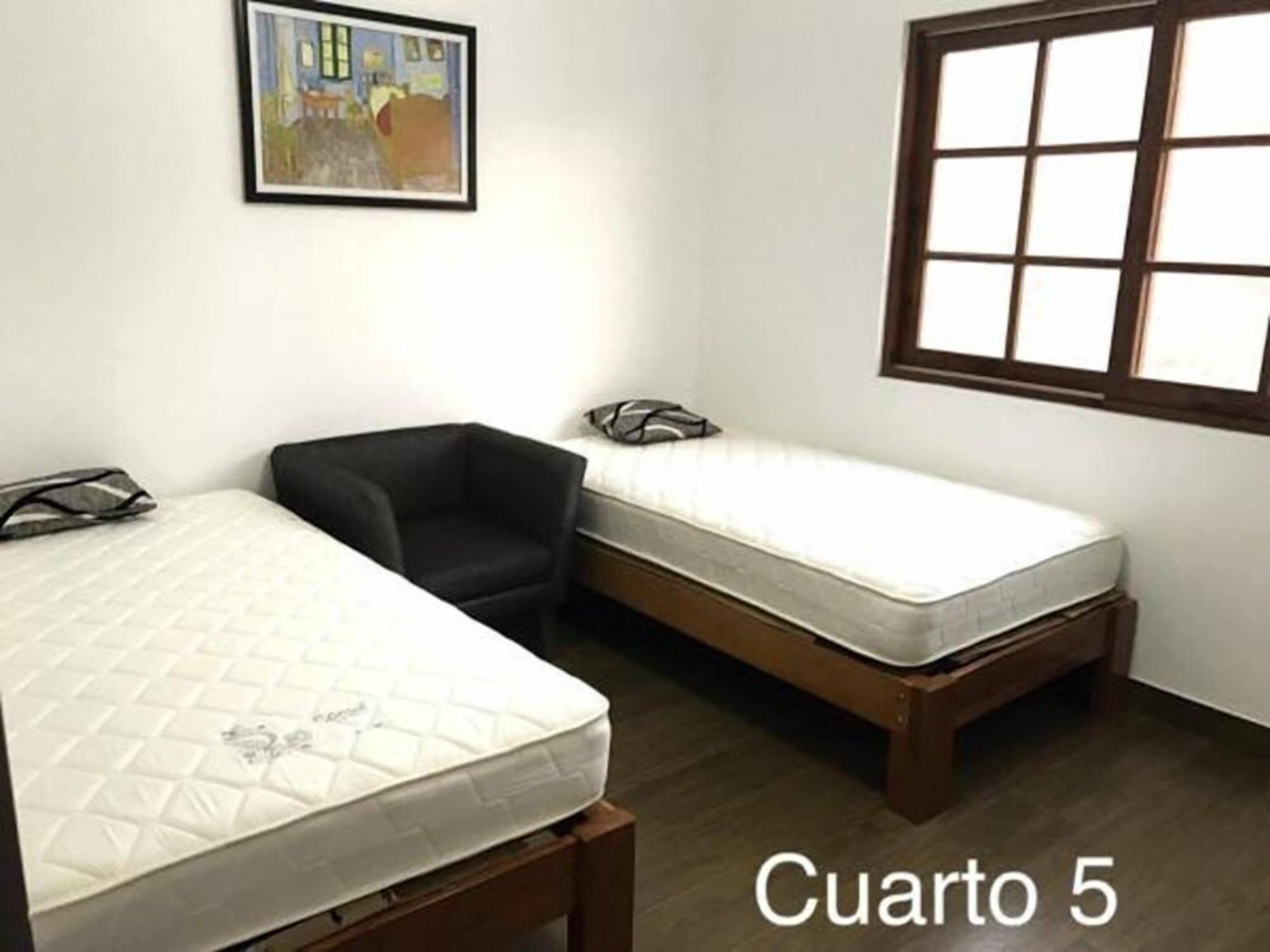 A room with two beds, a black chair, and a window with a grid pattern.