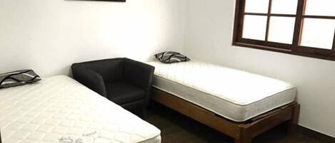 A room with two beds, a black chair, and a window with a grid pattern.
