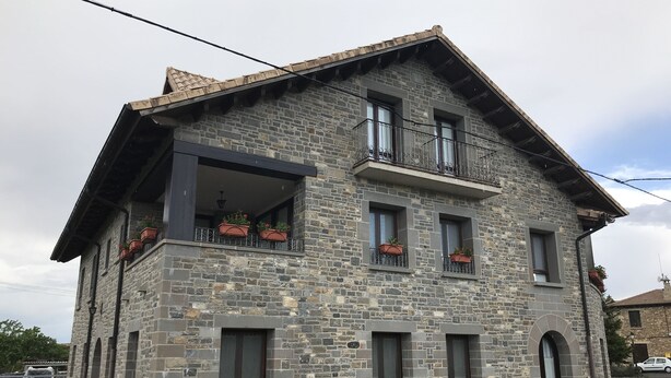 A stone building with multiple windows, a balcony with potted plants, and a small porch area.