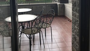 A balcony with a table and chairs, a hanging light fixture, and a view of houses and trees.
