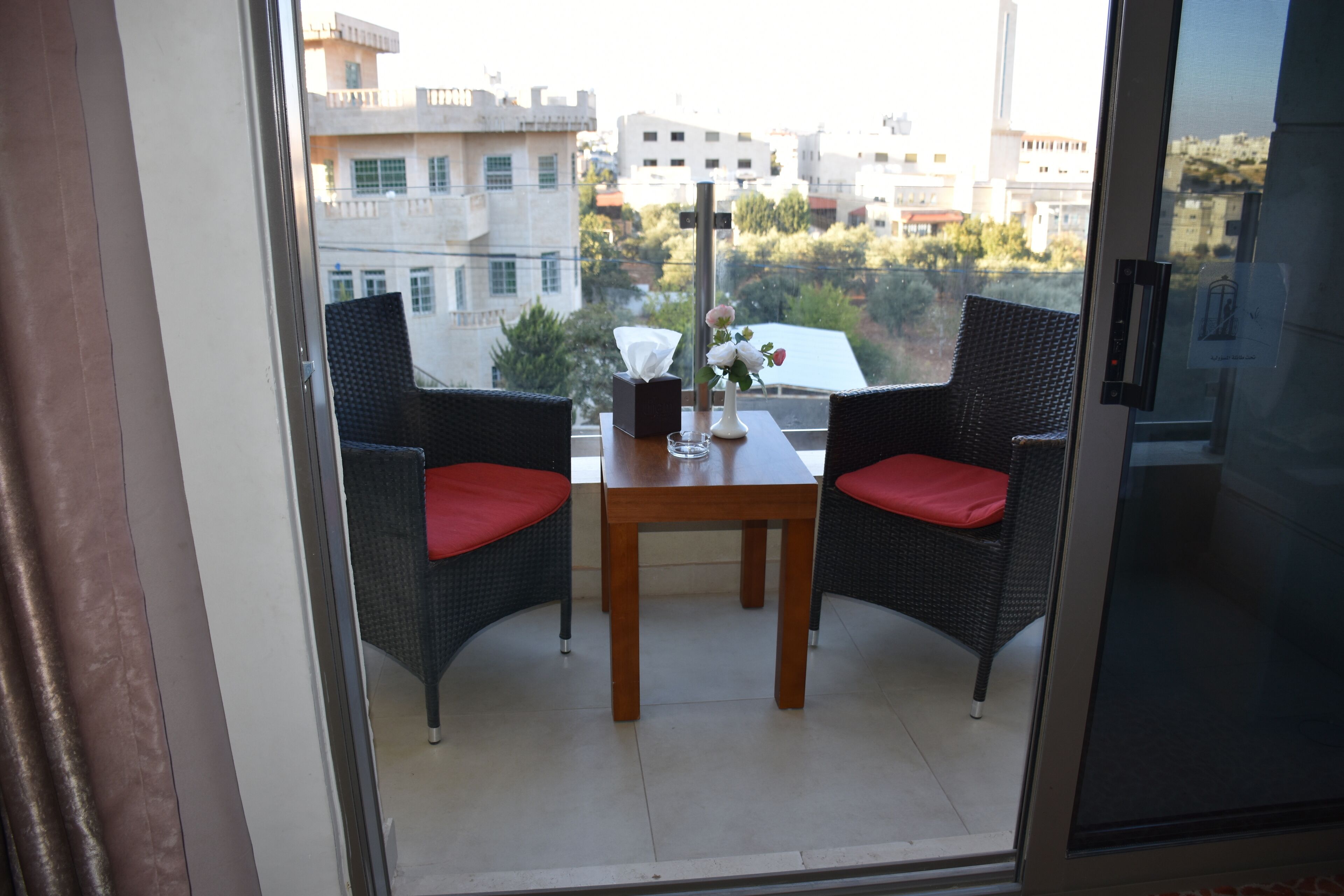 Un balcón con sillas de mimbre y una mesa, con vistas a un paisaje urbano.