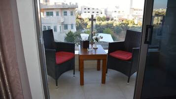 Un balcón con sillas de mimbre y una mesa, con vistas a un paisaje urbano.