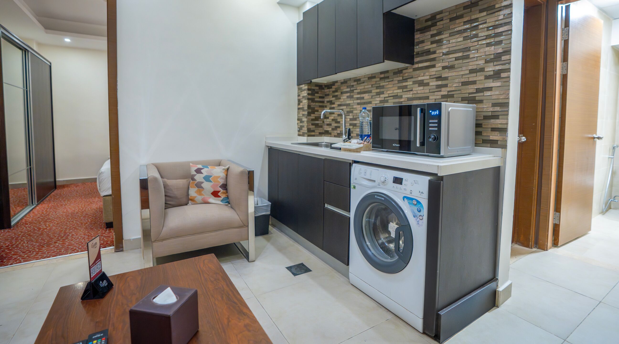 A compact living space with a sofa, a washing machine, a microwave, and a small kitchen area.