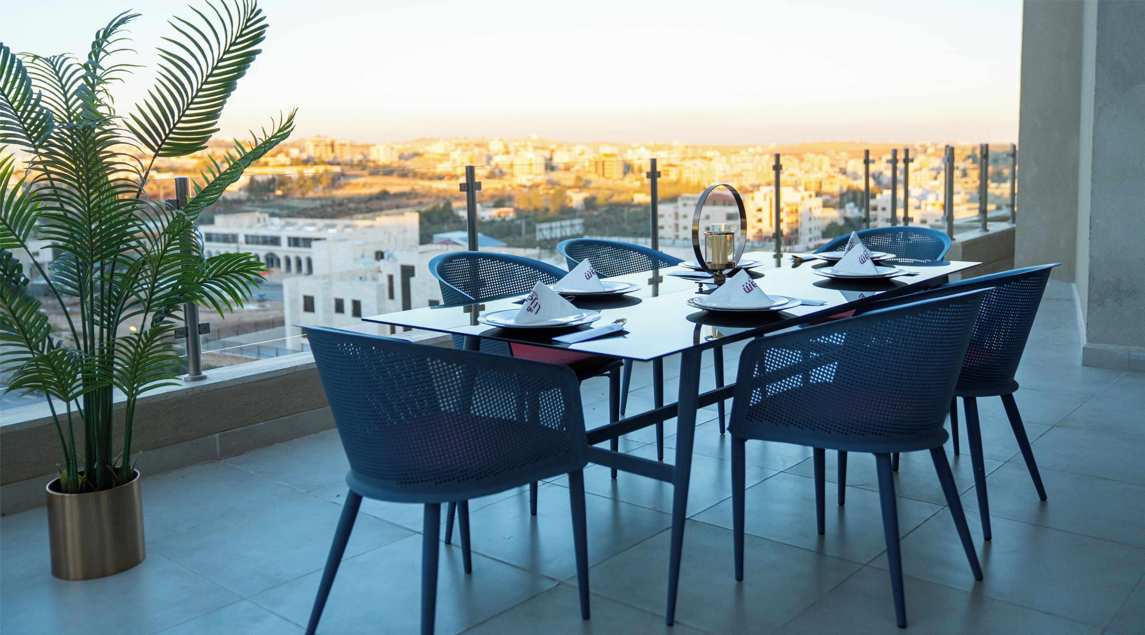 A dining area with a table set for four, chairs, a potted plant, and a city view.
