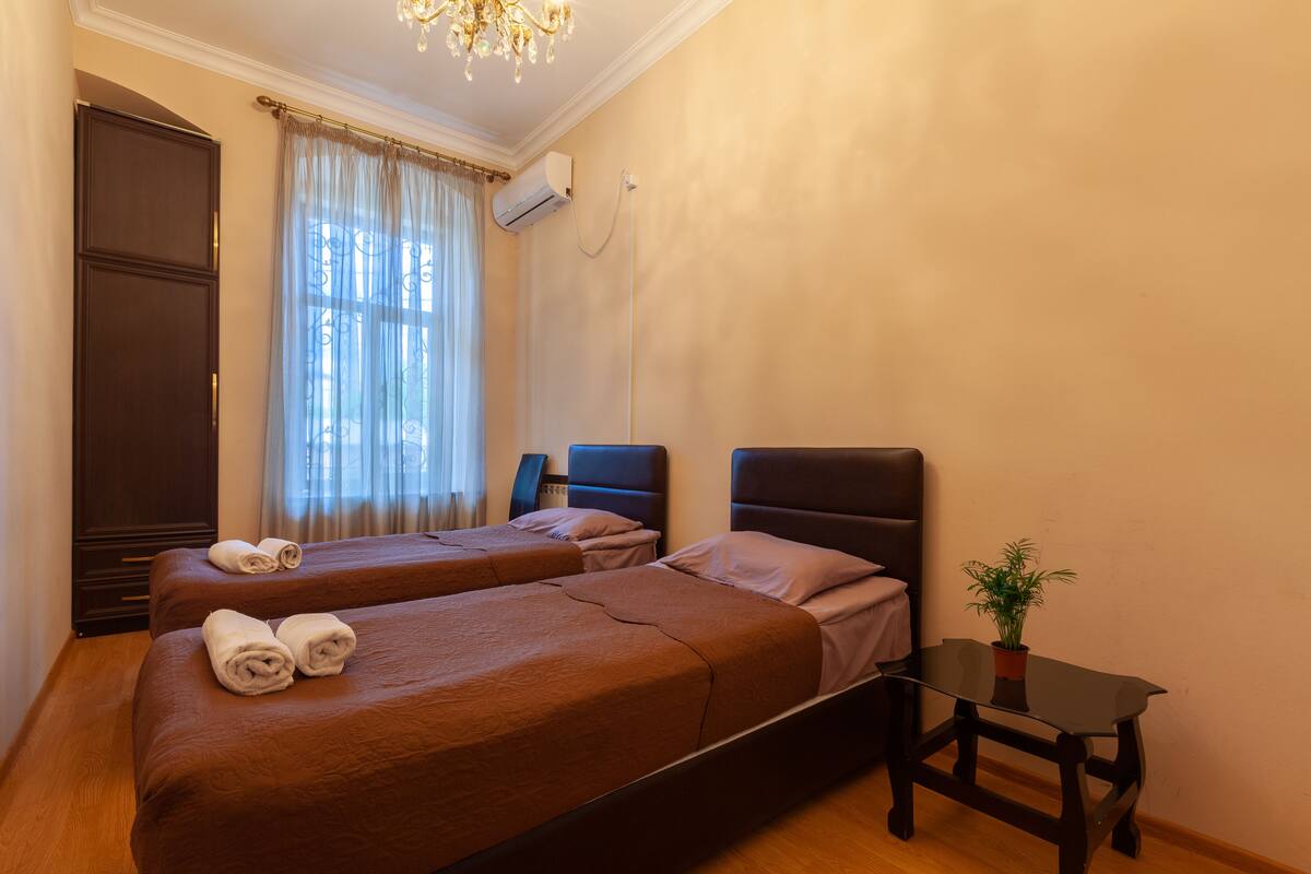 Een hotelkamer met twee bedden, een kleine tafel, een potplant en een raam met gordijnen.