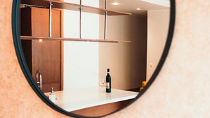 Casa de banho moderna com espelho redondo, bancada branca, uma garrafa de vinho e um copo.