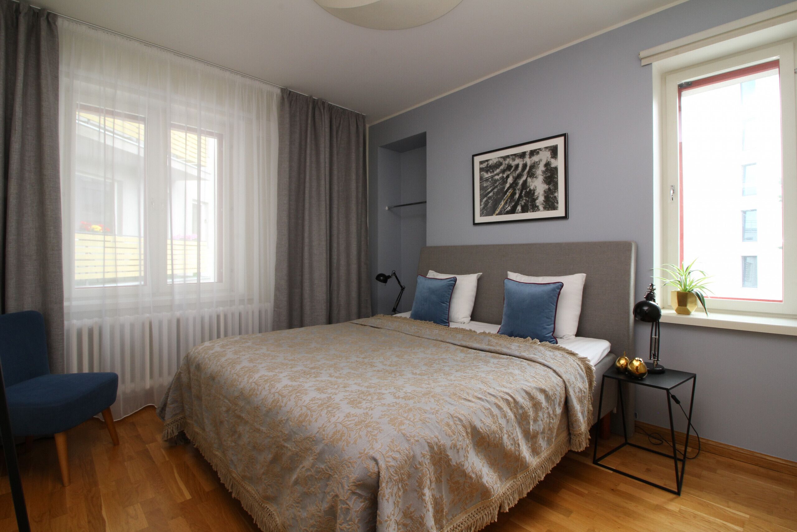 A bedroom with a large bed, a chair, a bedside table, a window with curtains, and a framed picture on the wall.