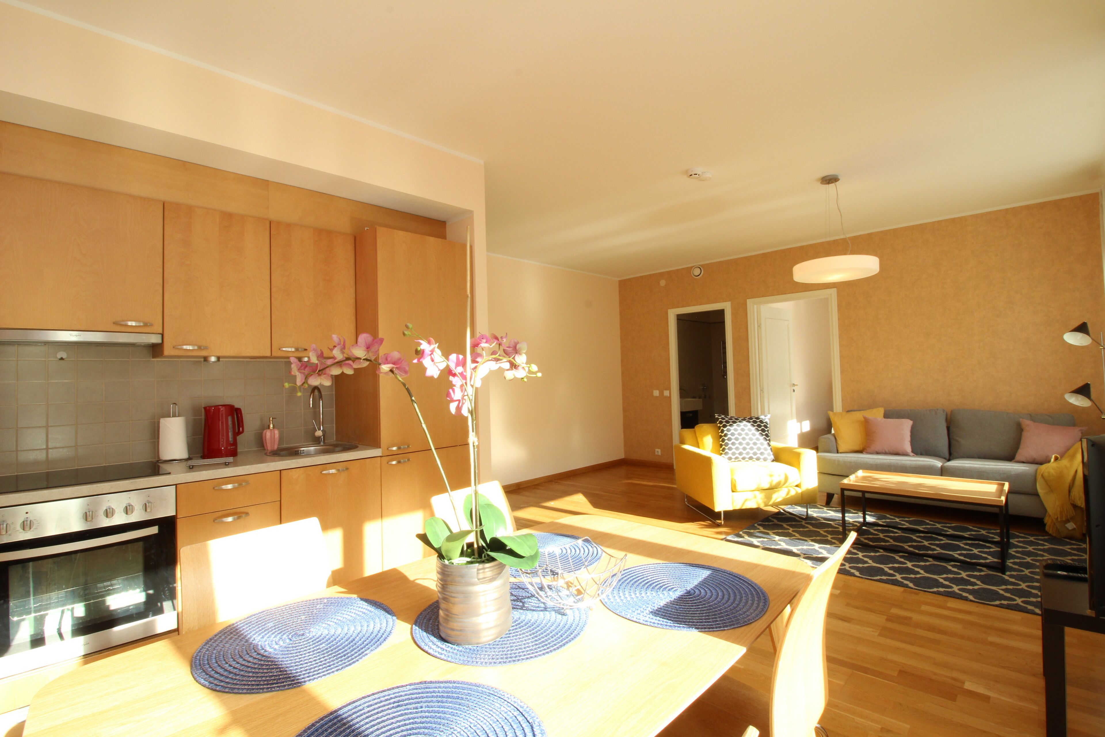 A modern kitchen with wooden cabinets, a stainless steel stove, and a dining area with a wooden table and blue placemats.