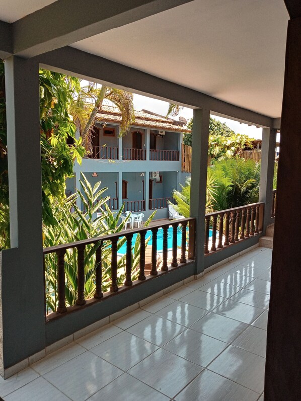 A covered balcony with a pool, surrounded by lush greenery and a two-story building with balconies. - Pousada Olhar da Sereia (Porto Seguro)