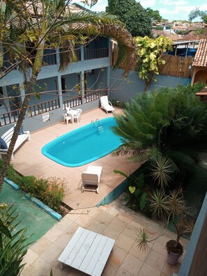 A swimming pool with lounge chairs, surrounded by lush greenery and a building with a blue exterior. - Pousada Olhar da Sereia (Porto Seguro)