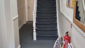 A staircase with a carpeted landing, a fire extinguisher, and a bulletin board on the wall. - Shamrock Guest House (Gravesend)
