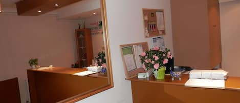 A reception desk with a mirror, a bulletin board, and a potted plant with pink flowers.