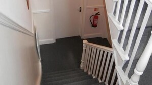 A staircase with white railings and a dark carpeted floor leading to a door marked with the number 6. - Shamrock Guest House (Gravesend)